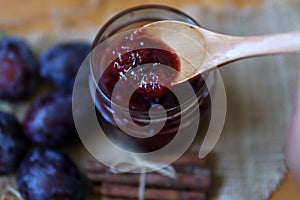 Plum jam in wooden spoon on glass jar in background