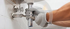 The plumber adjusting pipes under a bathroom sink using tools and gloves. AI generated image