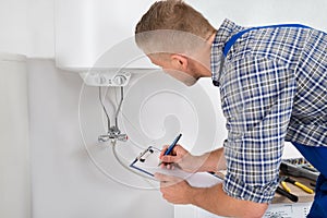Plumber With Clipboard In Front Of Electric Boiler