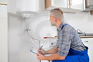 Plumber With Clipboard In Front Of Electric Boiler