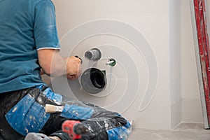 Plumber fitting a pipe in the bathroom. A man installing a toilet.