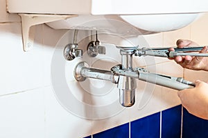 Plumber fixes sink siphon by two pipe-wrenche