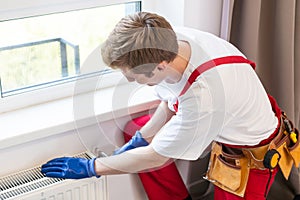 A plumber is fixing a radiator. With an adjustable wrench, he tightens the tap. A briefcase with a tool at hand