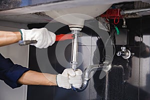 Plumber fixing white sink pipe with adjustable wrench