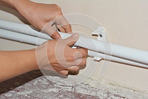 A plumber is installing central heating by laying new white polypropylene pipes into plastic waterline half clamps