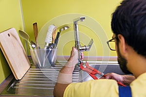 Plumber installing, repairing water tap in kitchen