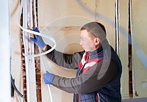 Plumber installs new plastic pipes in special boxes in the wall in house under construction