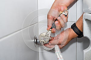 Plumber installs of a toilet hose in a hard-to-reach place with an adjustable wrench. photo