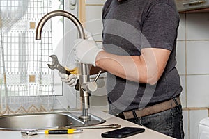 A plumber in the kitchen installs a new water tap. Repair of the faucet in the kitchen near the sink