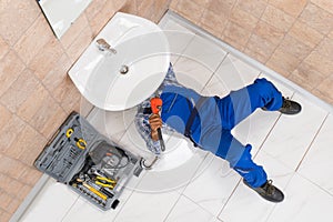 Plumber Lying On Floor Repairing Sink In Bathroom