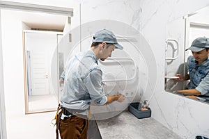 Plumber in medical mask installs electric heated towel rail in bathroom.