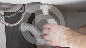 A plumber removes dirt from a siphon under a sink. Repair and eliminate leaks in the sink.