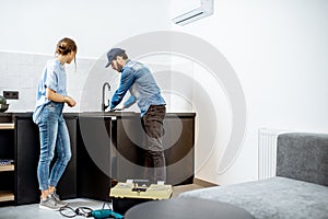 Plumber repairing kitchen faucet with woman in the apartment