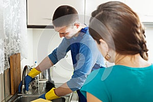 Plumber repairing kitchen sink for housewife