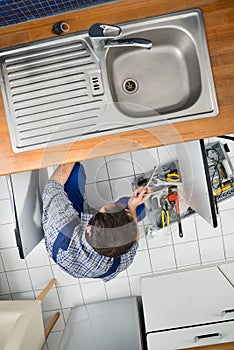 Plumber Repairing Sink In Kitchen