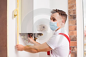 The plumber repairs a boiler in a medical mask