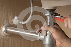Plumber repairs and maintains chrome siphon under the washbasin in bathroom. photo