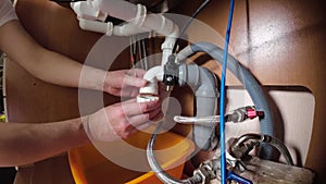 A plumber repairs pipes under a kitchen sink. He screws the pipes into place