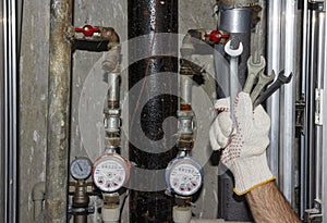 Plumber with spanners in sanitary unit. Hand plumbing with keys on background of pipes, manometers and filters in sanitary box