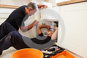 Plumber teaching an apprentice to fix a kitchen sink