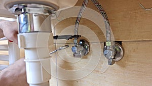 A plumber tightens the hose to the valve under the bathroom sink. The plumber's hands tighten the pipe to the water