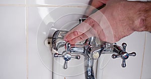 Plumber tightens nut with adjustable wrench during faucet installation.