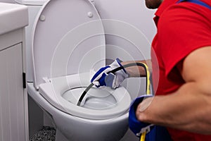 Plumber unclogging blocked toilet with hydro jetting at home bathroom. sewer cleaning service