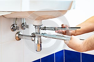 Plumber unscrews sink siphon by two pipe-wrenches
