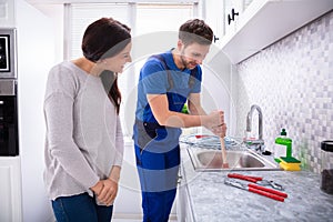 Plumber Using Plunger For Cleaning Kitchen Sink