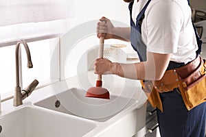 Plumber using plunger to unclog sink drain in kitchen, closeup