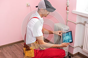 plumber at work. Installing water heating radiator with tablet