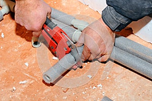 Plumber worker with scissors cuts the tube. cutting metal-plastic pipe by special red scissors. Plumber hands working