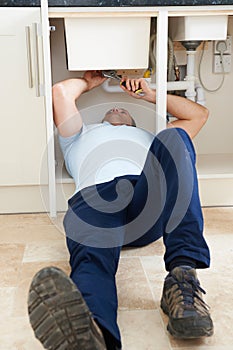 Plumber Working Under Sink With Wrench