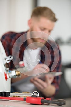 plumber writing in clipboard and checking electric boiler photo