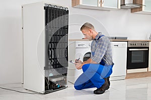 Plumber Writing On Clipboard In Front Of Refrigerator