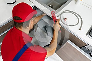 Plumbing services - plumber working in domestic kitchen, repairing sink pipes