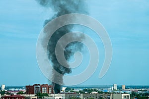 Plume of black smoke from a fire above city at sunset. Technogenic accident