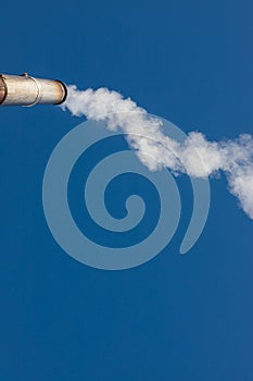 a plume of smoke or steam from an industrial smokestack on a clear blue sky