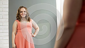 Plump lady looking in mirror with charming smile, self-confidence, body positive