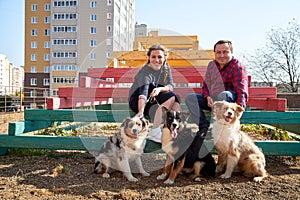Plump man and cute woman with dogs sitting on children colour stairs in city yard with big buildings background at summer sunny