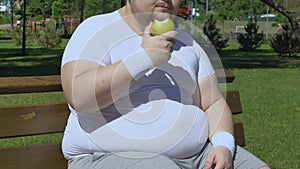 Plump man eating apple and sitting on bench, healthy low calorie snack, diet