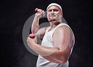 Plump man with red cheeks and a white bandage on his head lifts two red dumbbells and proudly looks at the camera