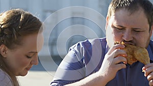 Plump woman eating salad while her obese boyfriend biting fatty fried chicken