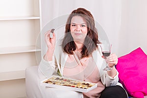 Plump woman at home eating chocolates and drinking wine photo