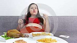 Plump woman sitting at a table and eating high-calorie junk food.Watching TV.