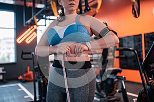 Plump woman wearing fitness tracker measuring waistline