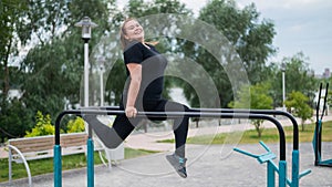 Plump young woman doing exercises on the uneven bars outdoors. Caucasian girl doing push-ups