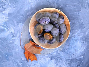 Plums in a bamboo bowl and a dry autumn leaf on a blue background