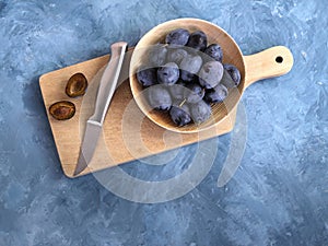 Plums in a bamboo bowl, a knife and a slit plum on a wooden board, a blue background