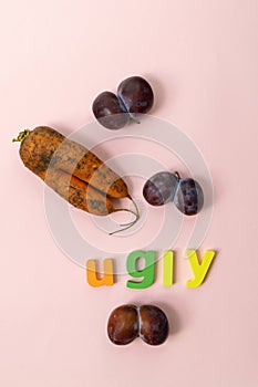 Plums and carrot fruit on pink background. Ugly fruit concept. Concept of beauty in uniqueness. Vertical photo